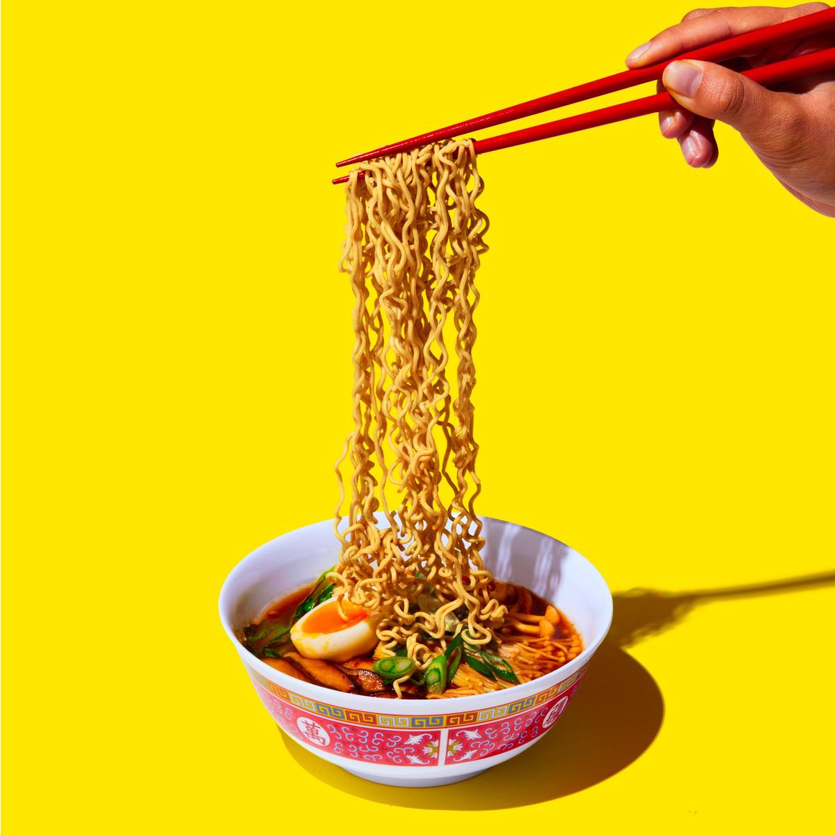 Chopsticks lifting immi noodles above a bowl on yellow